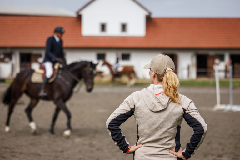 Female horse trainer supervising rider training before equestrian show jumping in paddock
